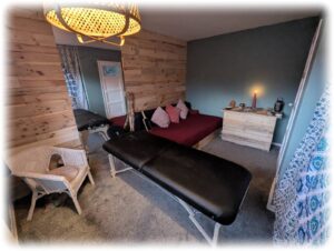 A warm, inclusive therapy room at Hummingbird Wing in Glasgow, featuring wood-paneled walls, a professional black massage table, a comfortable seating area, and soft ambient lighting with a lit candle for somatic and holistic sessions.